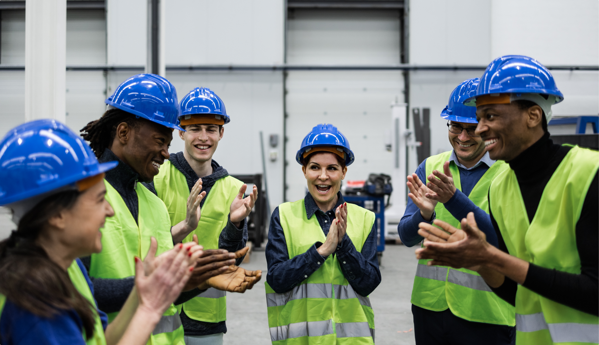 Workers in hard hats clapping and smiling.